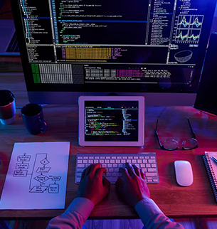 Profissional desenvolvendo site em computador, com códigos, telas abertas e fluxogramas na mesa, representando o serviço de desenvolvimento de sites da Birdclick.