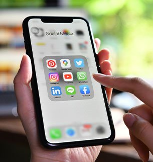 Pessoa segurando smartphone com aplicativos de redes sociais na tela, representando o serviço de gestão de mídias sociais da Birdclick.